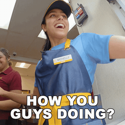 A Woman Wearing An Apron And A Name Tag That Says Michelle Is Smiling And Asking How You Guys Doing GIF