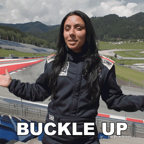 A Woman Wearing An Omp Jacket Is Standing In Front Of A Race Track GIF