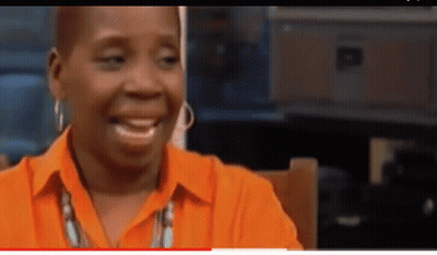 A Woman Wearing An Orange Shirt And Earrings Is Smiling . GIF