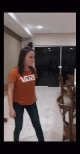 A Woman Wearing An Orange Vans Shirt Is Dancing In A Room GIF