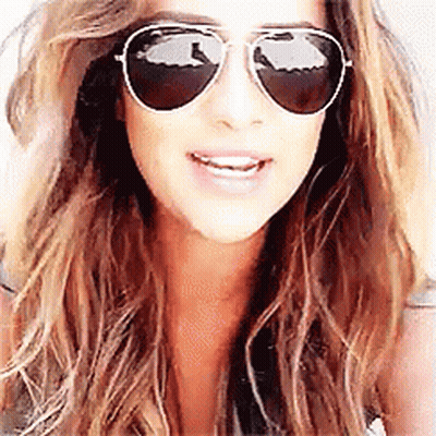 A Woman Wearing Aviator Sunglasses Is Smiling For The Camera . GIF