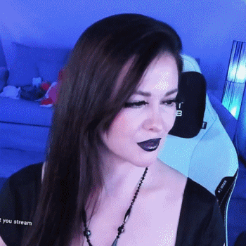 A Woman Wearing Black Lipstick And A Necklace Is Sitting In Front Of A Computer Screen That Says " You Stream " GIF
