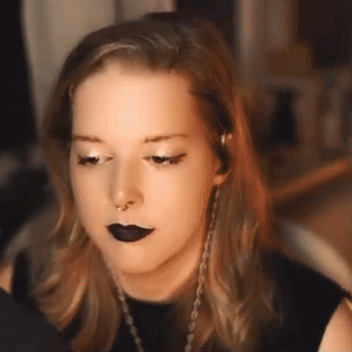 A Woman Wearing Black Lipstick And A Nose Ring Looks At The Camera . GIF