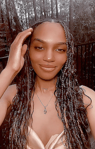 A Woman Wearing Braids And A Necklace Is Smiling For The Camera GIF