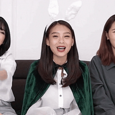 A Woman Wearing Bunny Ears And A Green Cape Is Sitting On A Couch With Two Other Women . GIF