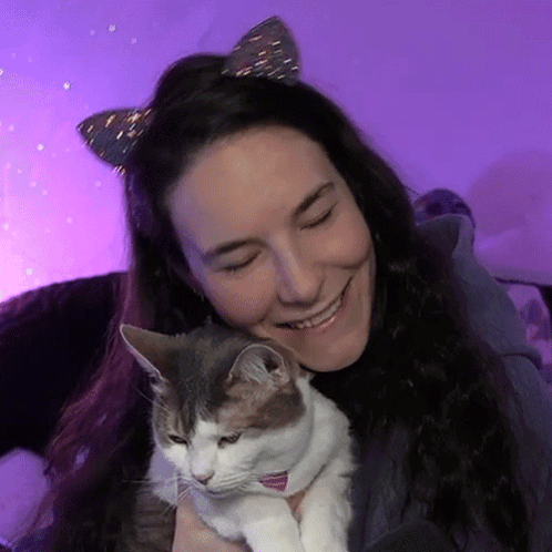 A Woman Wearing Cat Ears Is Holding A Cat In Her Arms GIF