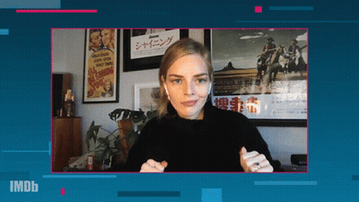 A Woman Wearing Ear Buds Stands In Front Of A Screen That Says Imdb On It GIF