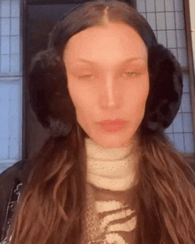 A Woman Wearing Ear Muffs And A Scarf Is Looking At The Camera . GIF