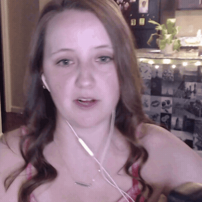 A Woman Wearing Earbuds And A Necklace Looks At The Camera GIF