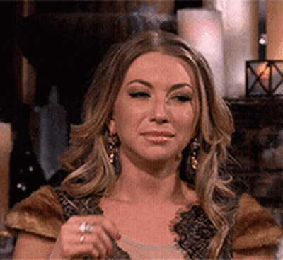 A Woman Wearing Earrings And A Ring Is Sitting In Front Of A Fireplace With Candles . GIF