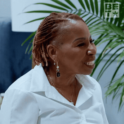 A Woman Wearing Earrings And A White Shirt Is Smiling In Front Of A Palm Tree GIF