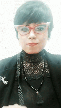A Woman Wearing Glasses , A Black Jacket , And A Black Necklace . GIF