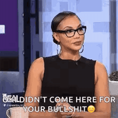 A Woman Wearing Glasses And A Black Dress Is Sitting In Front Of A Cup Of Coffee And Talking To Someone . GIF