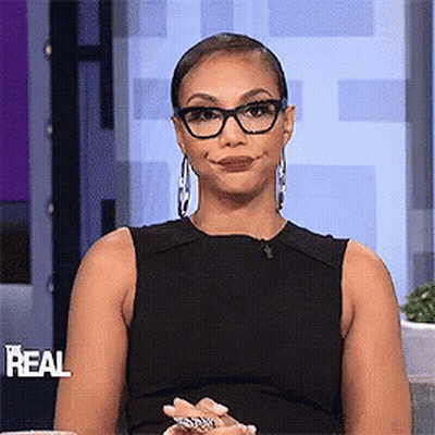 A Woman Wearing Glasses And A Black Dress Is Smiling And Making A Funny Face . GIF