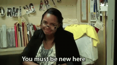A Woman Wearing Glasses And A Black Jacket Is Sitting At A Desk And Smiling . GIF