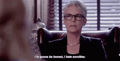 A Woman Wearing Glasses And A Black Jacket Is Sitting In A Chair And Talking To Someone . GIF