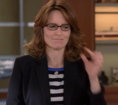 A Woman Wearing Glasses And A Black Jacket Is Smiling And Looking At The Camera . GIF