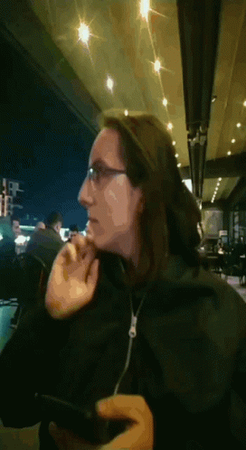 A Woman Wearing Glasses And A Black Jacket Looks At Her Phone GIF