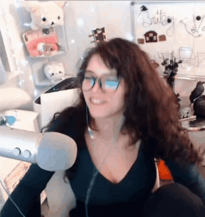 A Woman Wearing Glasses And A Black Shirt Is Sitting In Front Of A Microphone . GIF