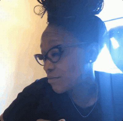 A Woman Wearing Glasses And A Black Shirt Looks Down At Something GIF