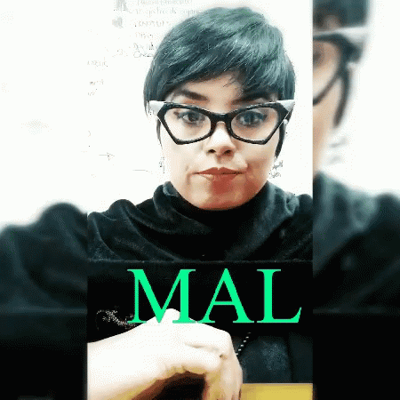 A Woman Wearing Glasses And A Black Turtleneck Is Holding A Sign That Says Mal On It GIF