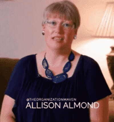 A Woman Wearing Glasses And A Blue Necklace Has The Name Allison Almond On Her Shirt GIF