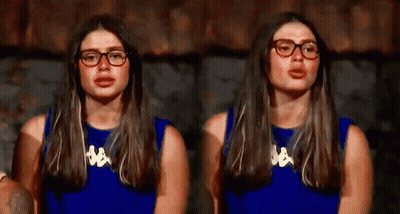 A Woman Wearing Glasses And A Blue Shirt Is Sitting In Front Of A Wall . GIF