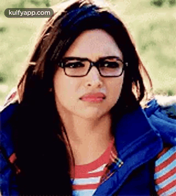 A Woman Wearing Glasses And A Blue Vest Is Making A Sad Face . GIF