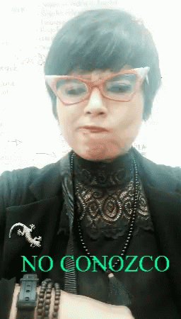 A Woman Wearing Glasses And A Brooch That Says No Conozco On It GIF