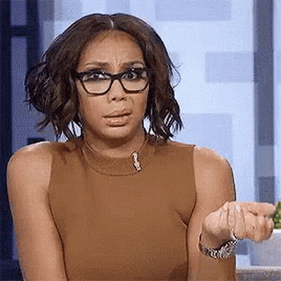 A Woman Wearing Glasses And A Brown Tank Top Is Making A Face . GIF