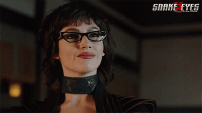 A Woman Wearing Glasses And A Choker With A Snake Eyes Logo Behind Her GIF