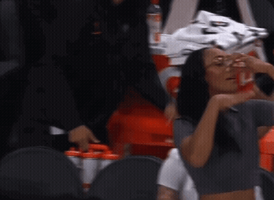 A Woman Wearing Glasses And A Crop Top Is Sitting In The Stands GIF