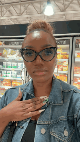 A Woman Wearing Glasses And A Denim Jacket Is Standing In Front Of A Fridge That Says ' Ii ' GIF