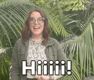 A Woman Wearing Glasses And A Green Jacket Is Standing In Front Of A Palm Tree And Smiling . GIF