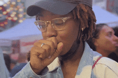 A Woman Wearing Glasses And A Hat Coughs GIF