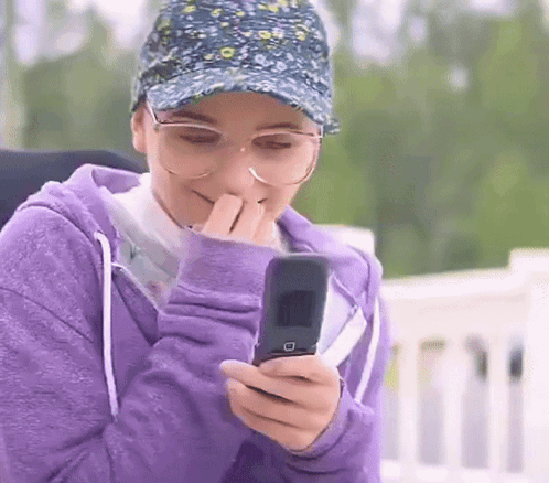 A Woman Wearing Glasses And A Hat Is Holding A Flip Phone . GIF