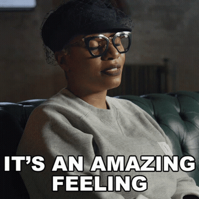 A Woman Wearing Glasses And A Hat Is Sitting On A Couch With The Words It 'S An Amazing Feeling Above Her GIF