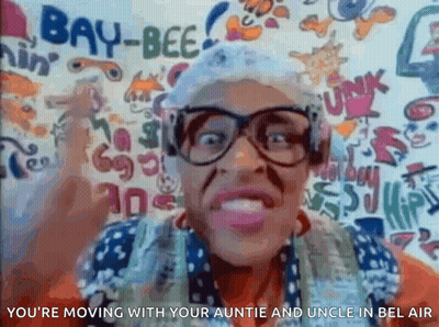 A Woman Wearing Glasses And A Hat Is Standing In Front Of A Wall That Has Graffiti On It . GIF