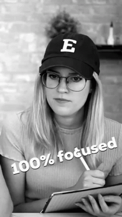 A Woman Wearing Glasses And A Hat With The Letter E On It Is 100 % Focused GIF