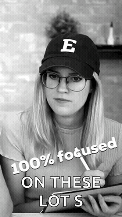 A Woman Wearing Glasses And A Hat With The Letter E On It Says 100 % Focused On These Lots GIF