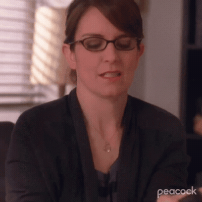 A Woman Wearing Glasses And A Necklace Is Sitting At A Table . GIF