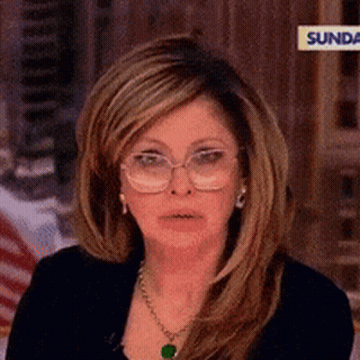 A Woman Wearing Glasses And A Necklace Is Sitting On A Sunday Show GIF