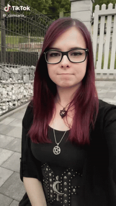 A Woman Wearing Glasses And A Necklace With A Pentagram On It Takes A Selfie GIF