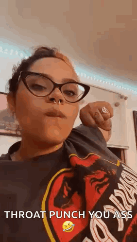 A Woman Wearing Glasses And A Nose Ring Is Giving A Throat Punch To The Camera . GIF