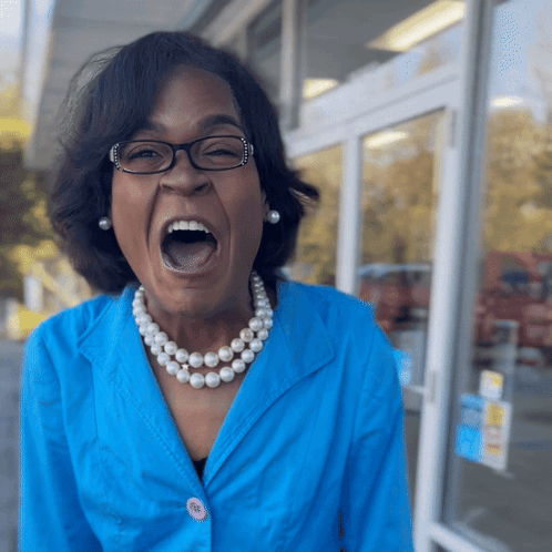 A Woman Wearing Glasses And A Pearl Necklace Screams With Her Mouth Open GIF