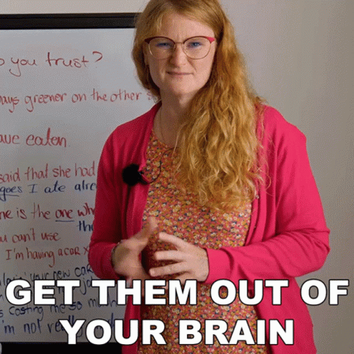 A Woman Wearing Glasses And A Pink Cardigan Stands In Front Of A White Board That Says Get Them Out Of Your Brain GIF