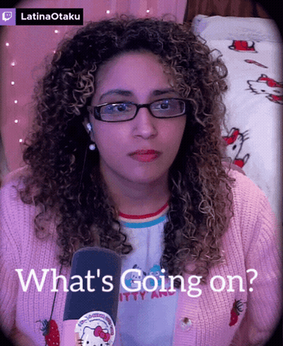 A Woman Wearing Glasses And A Pink Hello Kitty Sweater Says What 'S Going On In Front Of A Microphone GIF
