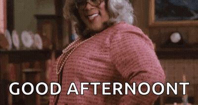 A Woman Wearing Glasses And A Pink Shirt Is Standing In A Living Room And Smiling . GIF