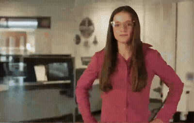 A Woman Wearing Glasses And A Pink Shirt Is Standing In A Room GIF