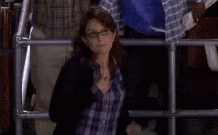 A Woman Wearing Glasses And A Plaid Shirt Is Standing In Front Of A Fence . GIF